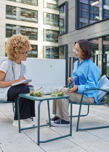 Diverse women cooperate during workday discuss marketing plan for startup project hold digital table